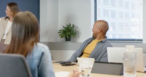 Diverse Team Collaborating and Listening in Modern Meeting Room with Laptops