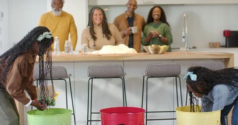 Multigenerational family laughing while children playing bucket game at kitchen island