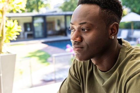 African american man sitting on patio looking thoughtful by modern backyard pool