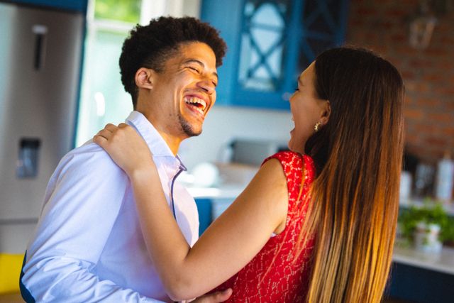 Young biracial couple enjoying a joyful moment dancing together in their home. Perfect for use in articles or advertisements about relationships, love, and lifestyle. Ideal for promoting home decor, family life, or romantic getaways.