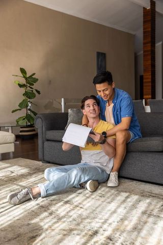 Male couple sharing notebook and laughing while relaxing in bright modern living room