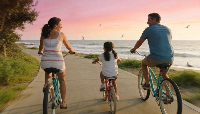Family biking along coastal promenade at sunset with parents and child on cruisers