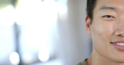 Closeup asian man smiling calmly near window with soft bokeh light, natural indoor headshot
