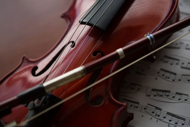 This image shows a close up of a brown violin resting on sheet music on a table. Ideal for use in educational materials, music school promotions, classical music event flyers, and articles about learning musical instruments.
