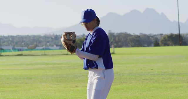 Baseball player in blue and white uniform concentrating before pitching in an open field with distant mountains in the background. Ideal for sports and fitness publications, athletic training materials, youth baseball promotions, and competitive sports advertising.