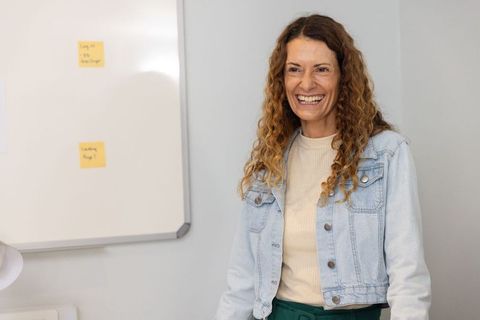 Mature woman laughing during office workshop by whiteboard, denim jacket portrait