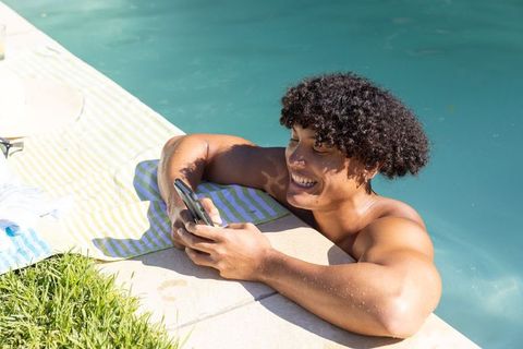 Smiling man texting at pool edge with striped towel and sunglasses, sunny summer leisure