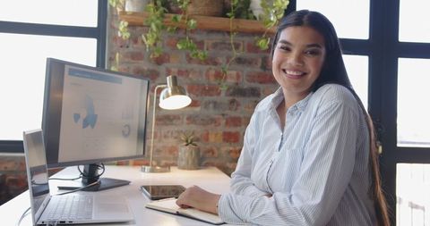 Businesswoman Smiling at Desk in Modern Office with Laptop and Charts