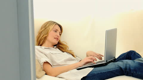 Woman Relaxing on Sofa while Using Laptop at Home