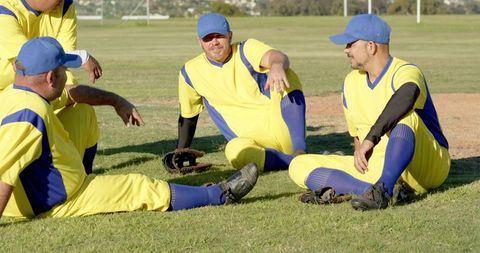 Community baseball team relaxing on grass after game in yellow and blue uniforms