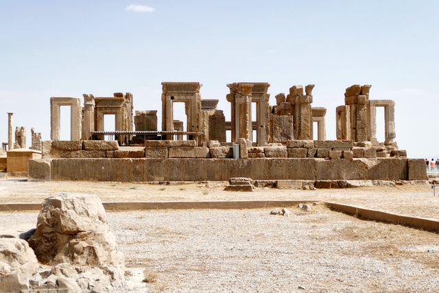Ancient ruins from the Achaemenid Empire featuring stone columns and structures under a clear blue sky. Ideal for content about ancient history, archaeological studies, travel destinations, cultural heritage, and historical education.