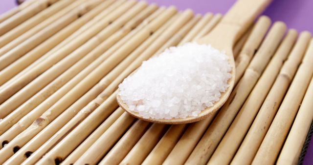 A wooden spoon filled with white granulated sugar rests on a bamboo mat, with copy space. Sugar is a common sweetener used in various culinary applications around the world.