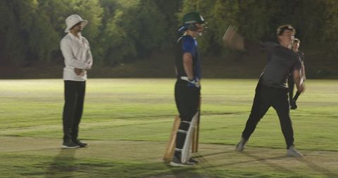 Evening cricket match bowling moment with white teen bowler delivering ball, batsman and umpire