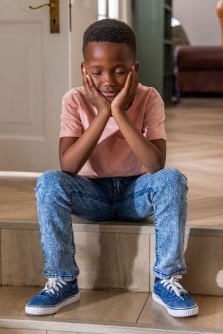 African american boy sitting on steps in home entry, eyes closed, calm contemplation