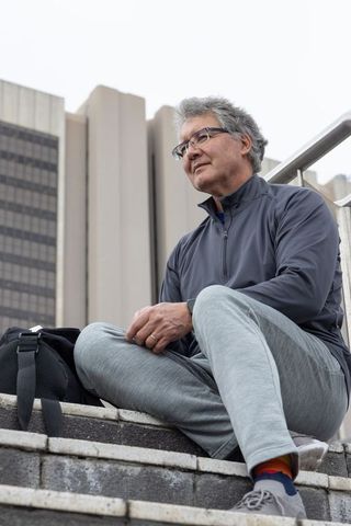 Senior man sitting on concrete steps contemplating city life with backpack