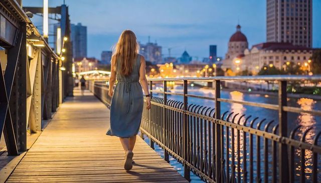 Woman walking riverside bridge at dusk with city lights reflecting on water