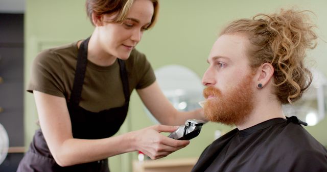Female barber carefully trimming beard for male client in modern salon. Ideal for showcasing professional grooming services, beauty industry, skilled barbers, personal care routines, and client-barber interactions.