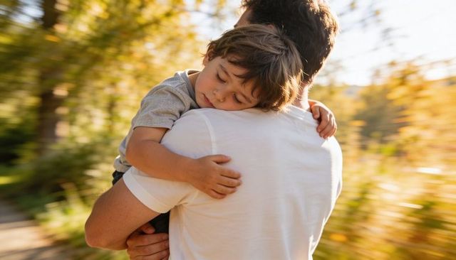 Father carrying sleeping son during golden hour in sunlit park