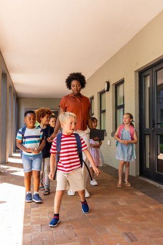 Teacher leading diverse elementary students walking through sunlit school corridor