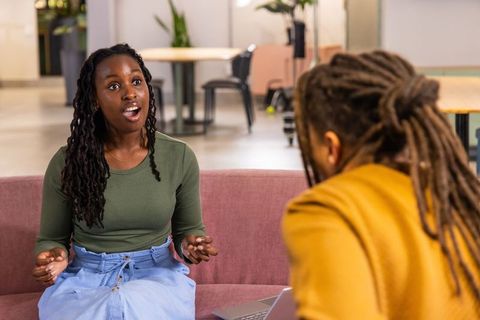African american coworkers discussing project on sofa in modern open-plan office lounge