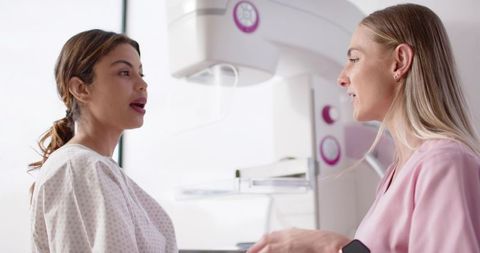 Clinician consulting patient at mammography unit while preparing breast imaging appointment