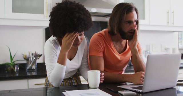 Stressed biracial couple using laptop and calculating finances in the kitchen at home. staying at home in self isolation in quarantine lockdown