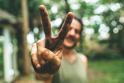 Smiling Gardener Showing Peace Sign with Muddy Fingers Outdoors