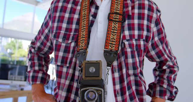 Caucasian man stands with a vintage camera, with copy space. He's a photography enthusiast or professional in a bright indoor setting.