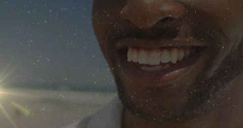 Smiling man wearing light collar and stubble at sunlit shoreline close-up with sun flare