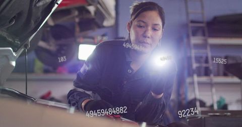 Woman mechanic inspecting car engine, shining flashlight with diagnostic data overlays