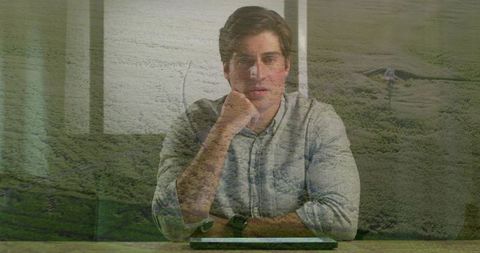 Contemplating businessman resting chin on fist at desk with tablet and landscape overlay