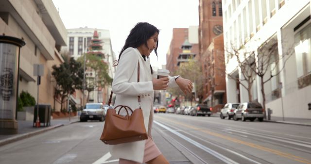 Businesswoman walks briskly on city street, holding coffee, checking time on wristwatch. This image conveys a busy, urban lifestyle, perfect for use in contexts relating to business, hustle, urban living, and time management.