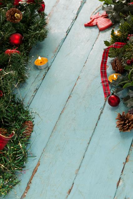 Christmas decorations including a tealight candle, wreaths, pine cones, and ornaments arranged on a rustic wooden plank. Ideal for holiday greeting cards, festive invitations, seasonal blog posts, and Christmas-themed marketing materials.