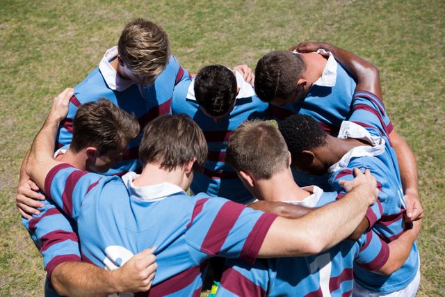 High angle view of rugby team making  huddle while standing at playing field on sunny day 
