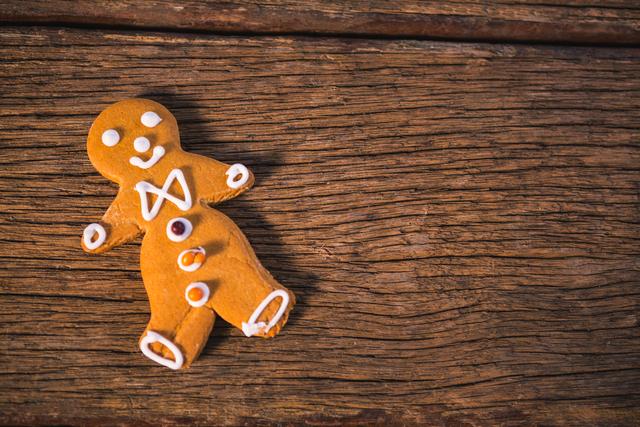 Gingerbread man with icing decoration lying on a rustic wooden table. Ideal for holiday-themed designs, Christmas cards, festive advertisements, and baking blogs. Perfect for conveying a warm, traditional holiday atmosphere.
