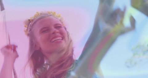Carefree woman swinging with flower crown under pastel sky, joyful summer moment