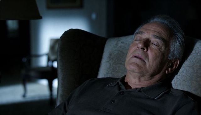 Senior man sleeping in armchair at night with soft lamp light, cozy restful home interior