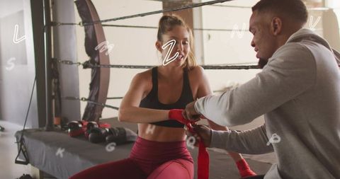 Female boxer receiving hand wraps from trainer at boxing ring apron during training session