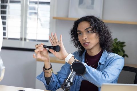 Non-binary beauty creator demonstrating makeup brush technique on-camera in home studio
