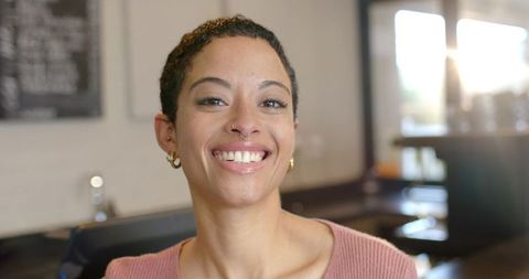 Smiling barista in modern coffeehouse wearing septum ring and pink knit top, natural light