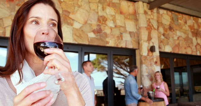 Woman enjoying wine outdoors with friends socializing in the background - Download Free Stock Images Pikwizard.com