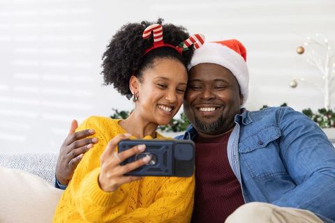 African American couple taking joyful Christmas selfie on couch wearing Santa hats