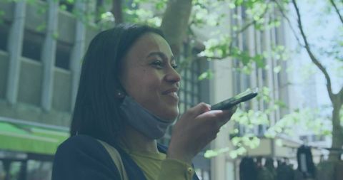 Woman using smartphone for voice message on city sidewalk