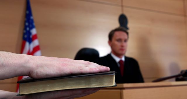 A person is taking an oath in a courtroom, with a focus on the hand on the Bible and a Caucasian judge in the background. The scene represents a pivotal moment in legal proceedings, emphasizing the solemnity of courtroom oaths.