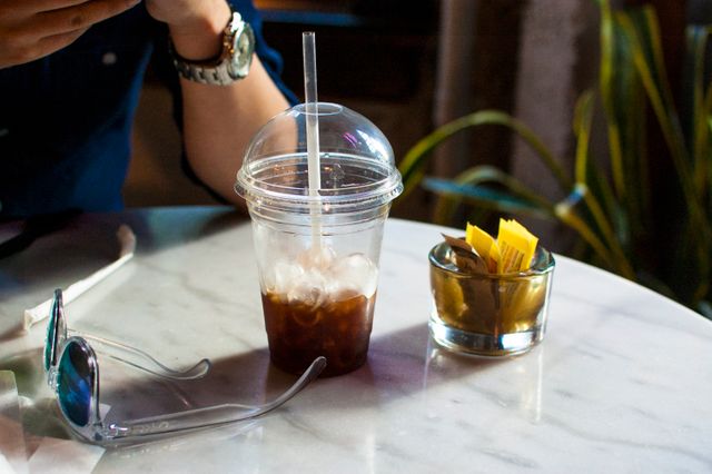 Man Enjoying Iced Coffee at Café Table with Sunglasses and Sweeteners - Download Free Stock Images Pikwizard.com