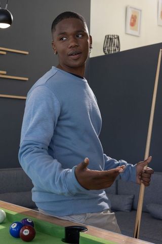 African american male holding cue at modern lounge pool table, relaxed social recreation
