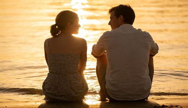 Couple sitting on sunset beach watching golden sea together romantic evening moment