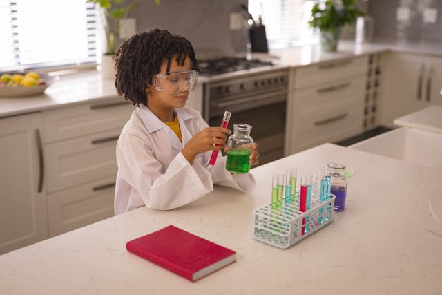 Hispanic boy wearing safety goggles and lab coat conducting a science experiment in a modern kitchen. He is mixing a green chemical solution in a beaker with a test tube. Ideal for educational content, STEM promotion, children's learning materials, and science-related articles.