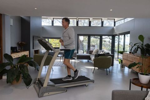 Man Exercising on Treadmill in Modern Living Room with Tree Views