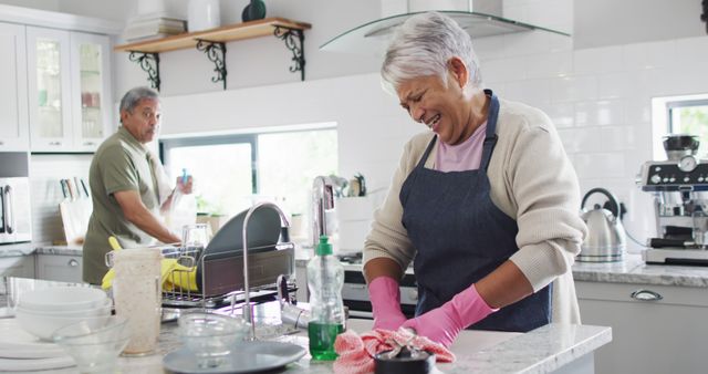 Elderly couple smiling and cleaning together in the kitchen, promoting themes of family life, teamwork, and active senior living. Useful for content on aging gracefully, home routines, and family togetherness.